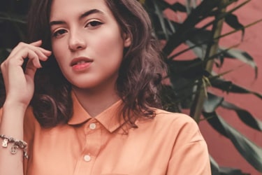 Lady posing by a red wall with a plant between them